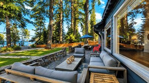 A patio with outdoor seating, stone walls, and a view of the forest. - West Shore Lake House by Avantstay Ski Cabin w/ Backyard Sledding Hill! (Homewood)
