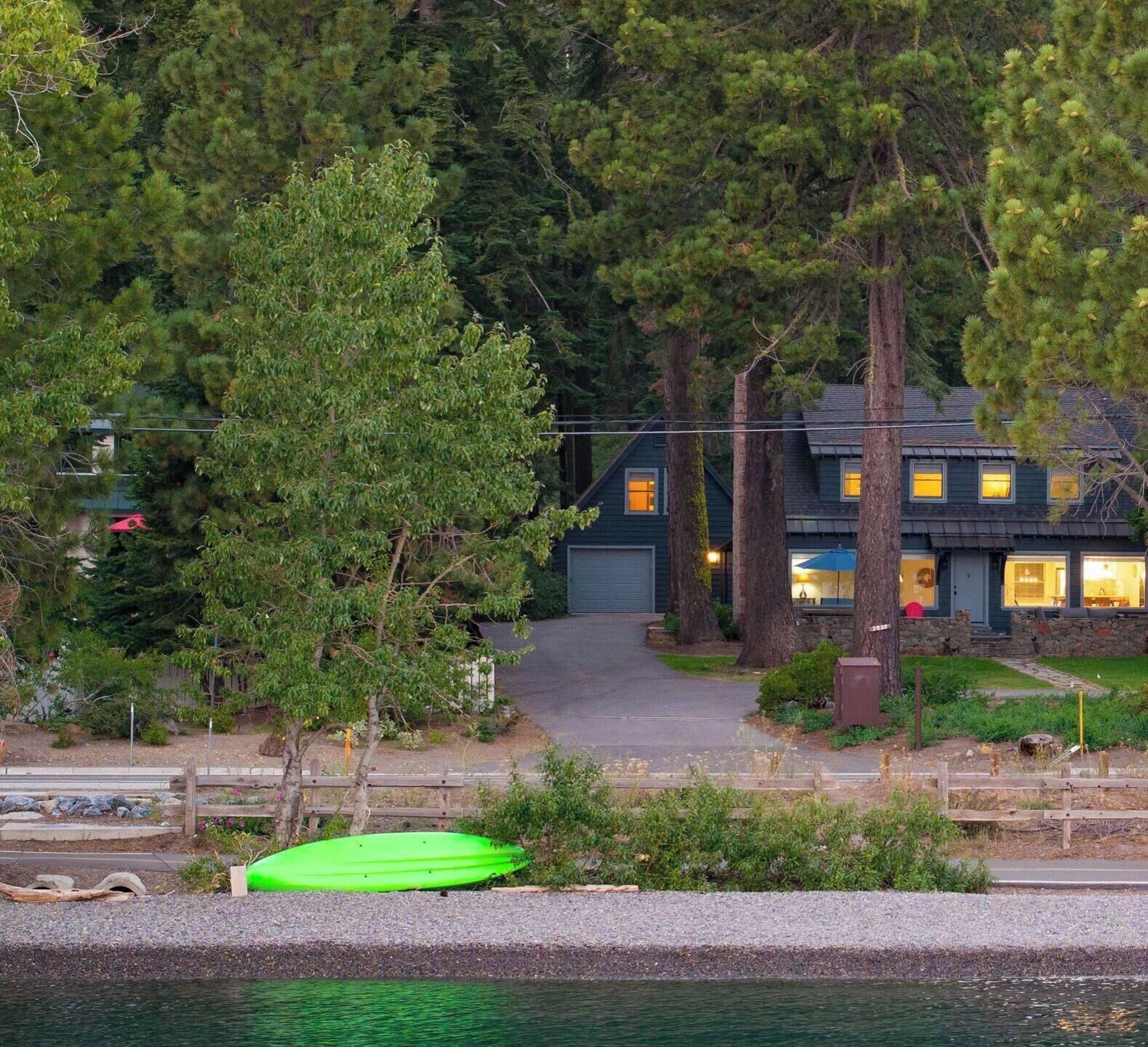 A house with a driveway leading to a garage, surrounded by dense trees and a body of water.