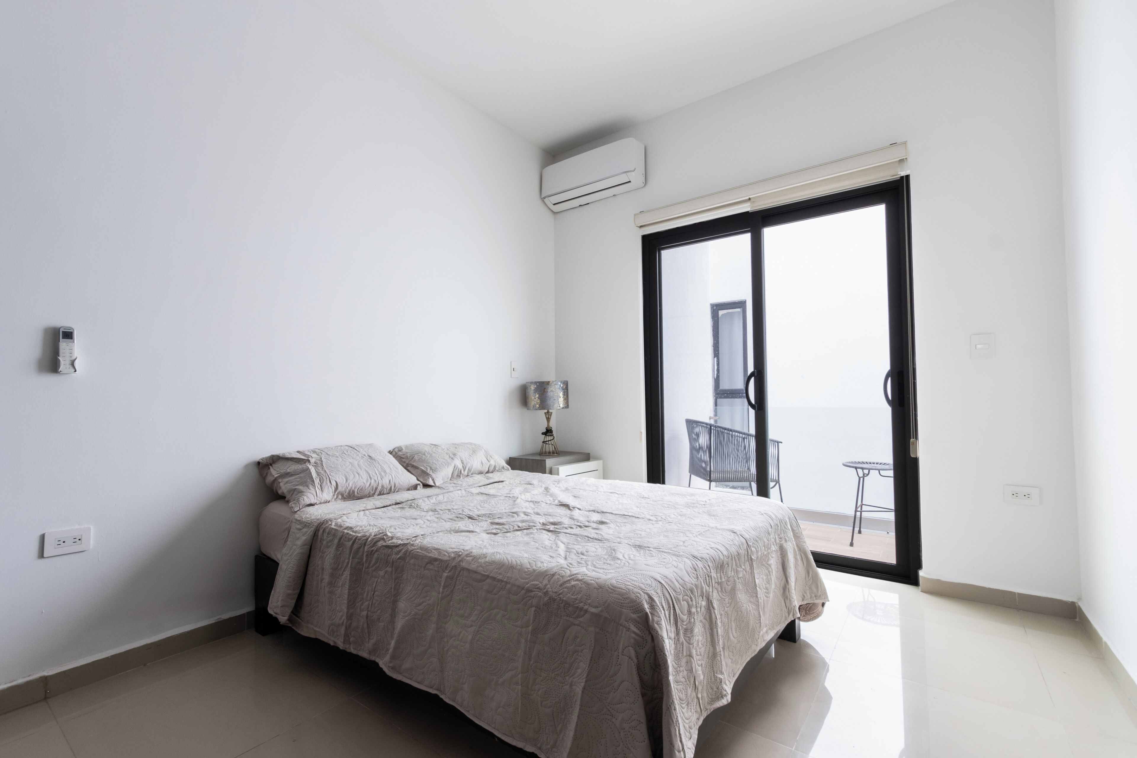 Een slaapkamer met een bed, nachtkastje, lamp en een schuifdeur naar een balkon.