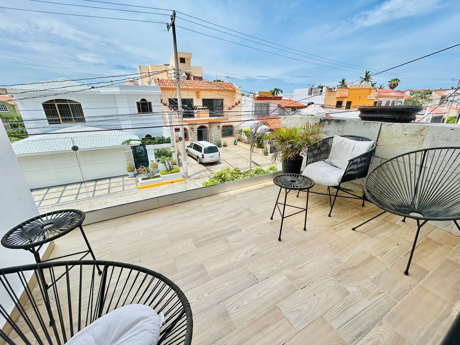 A balcony with two black wire chairs, a small round table, and a white sofa. A white van is parked on the street below.