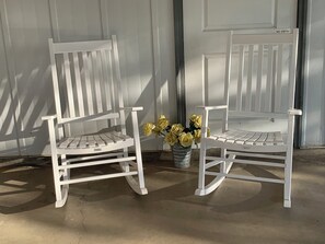 Twee witte schommelstoelen met een metalen emmer vol gele bloemen ertussen.