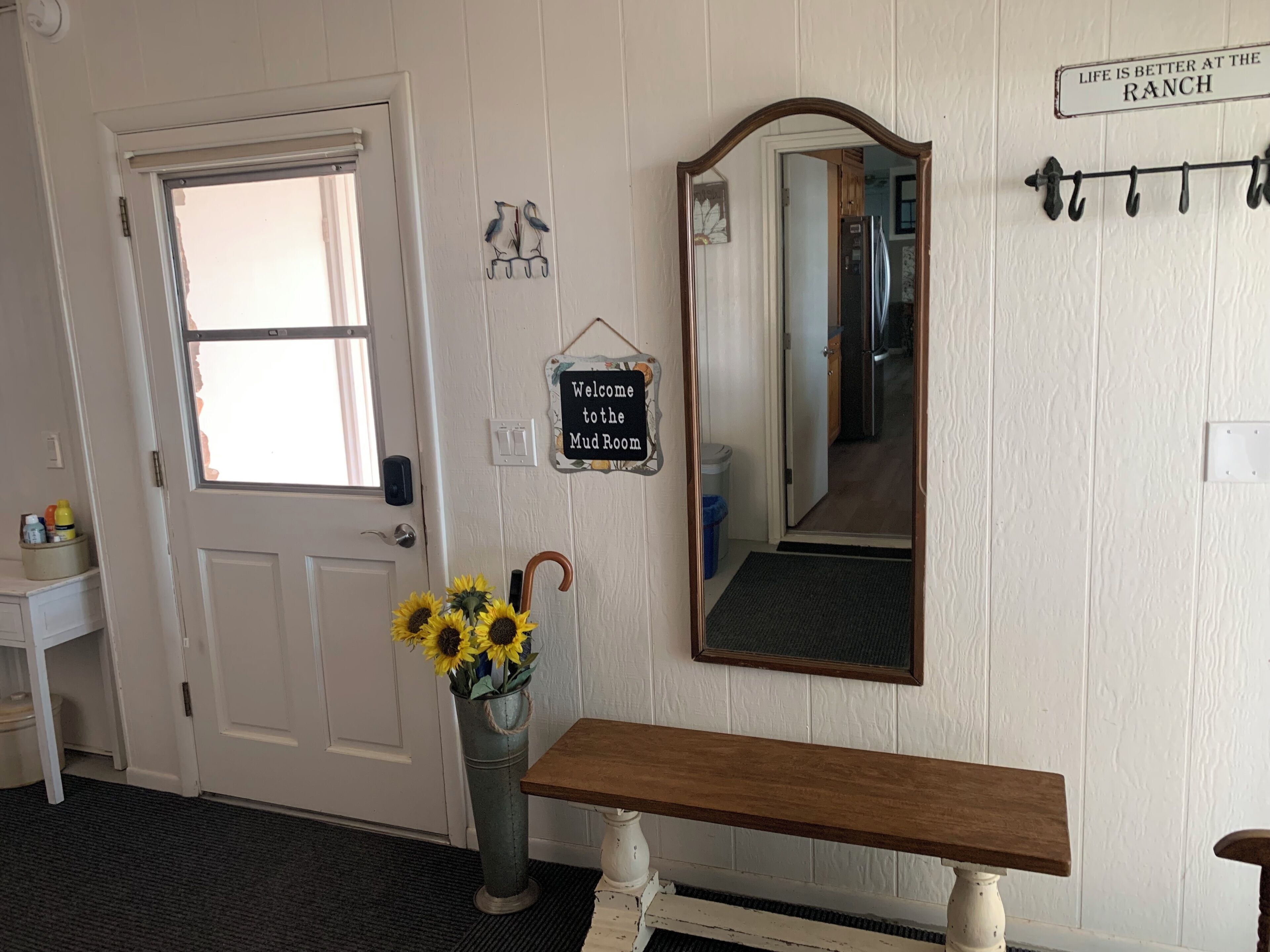 A room with a white door, a bench, a mirror, and a welcome sign.