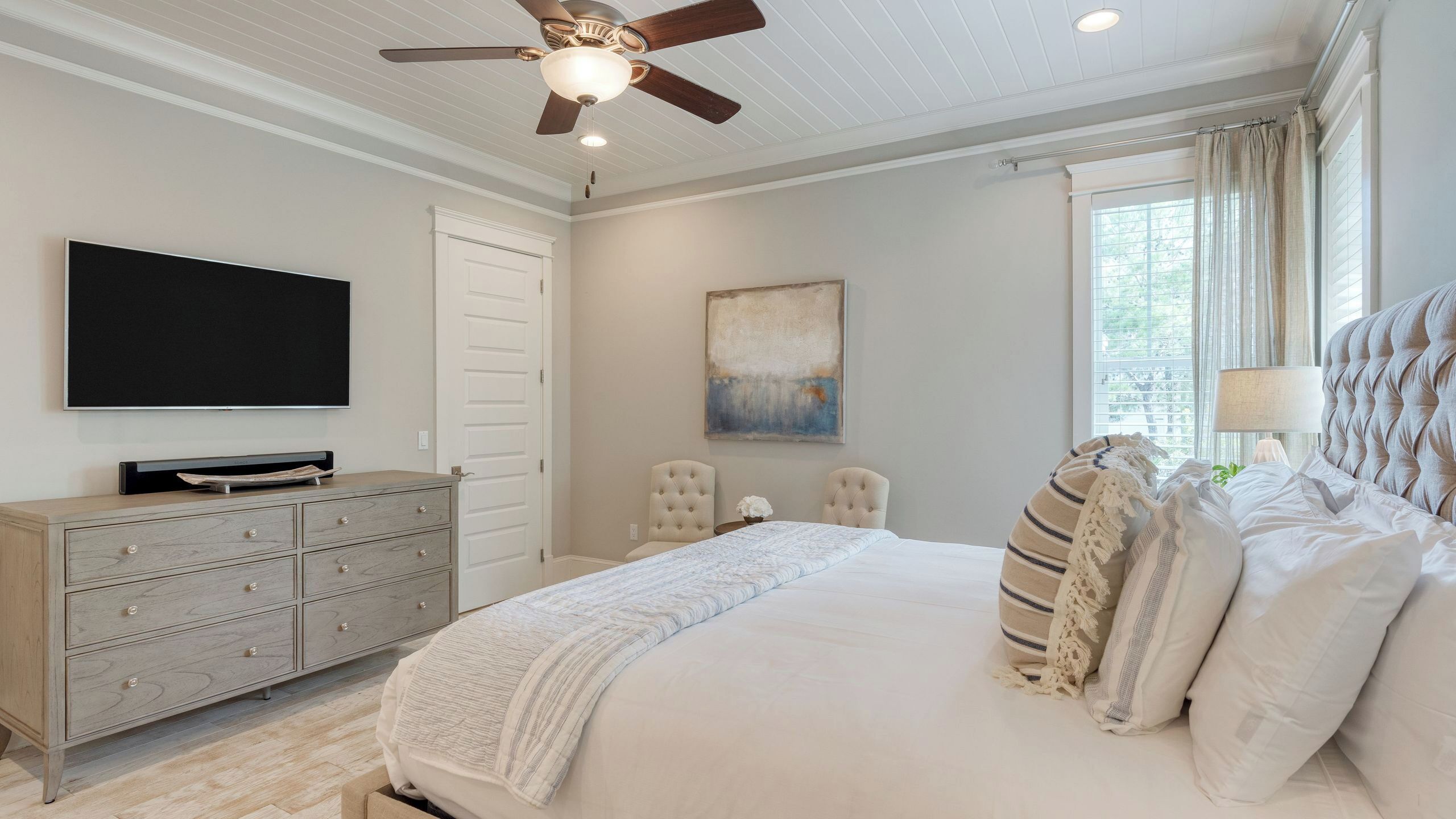 A bedroom with a bed, dresser, TV, ceiling fan, and artwork.
