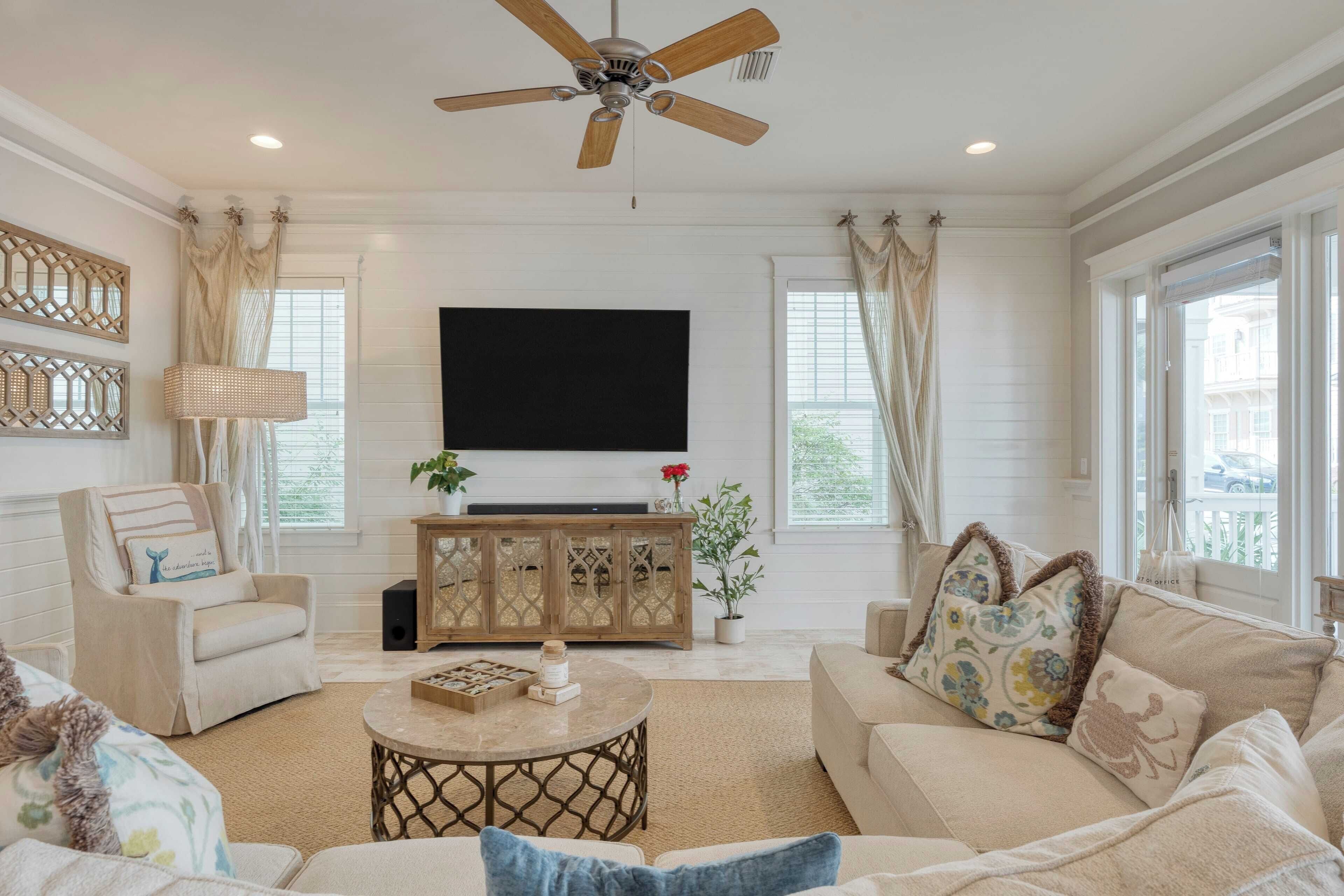 Un salon doté d’un ventilateur de plafond, d’un téléviseur à écran plat, d’un meuble en bois et d’un canapé beige.