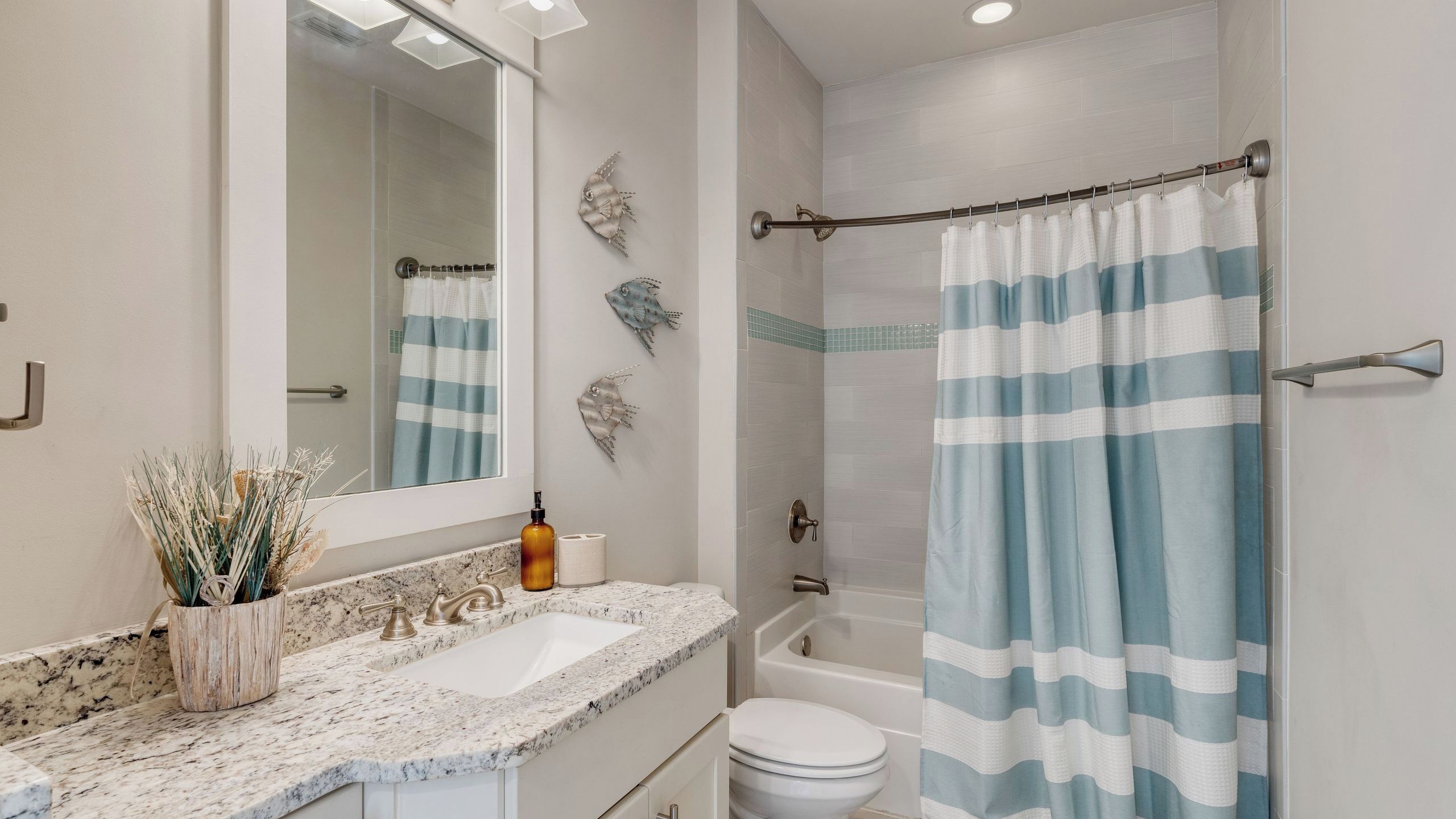A bathroom with a sink, mirror, toilet, shower, and a towel rack.