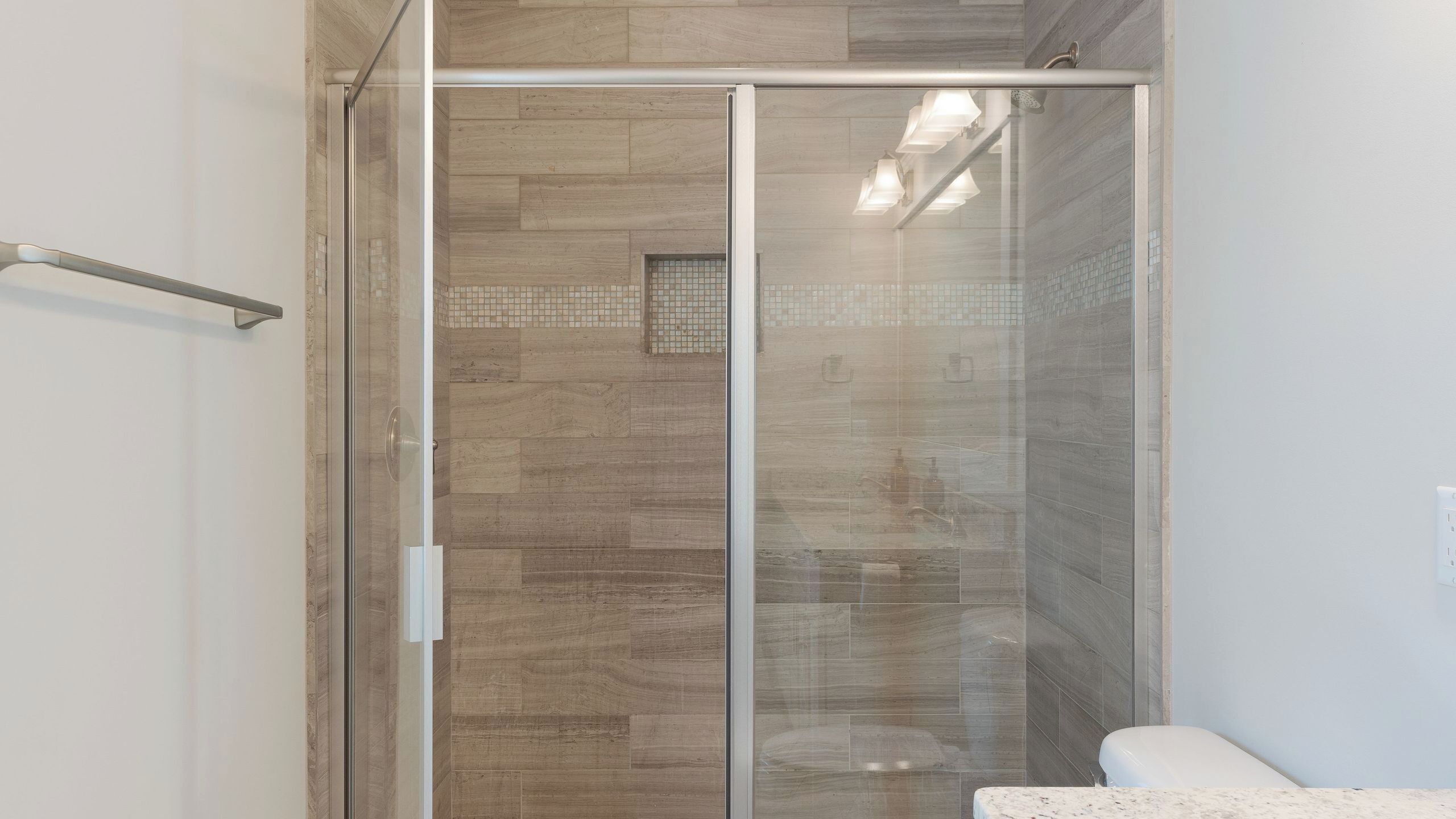 A modern bathroom with a glass shower enclosure, a white sink, and a tiled floor.