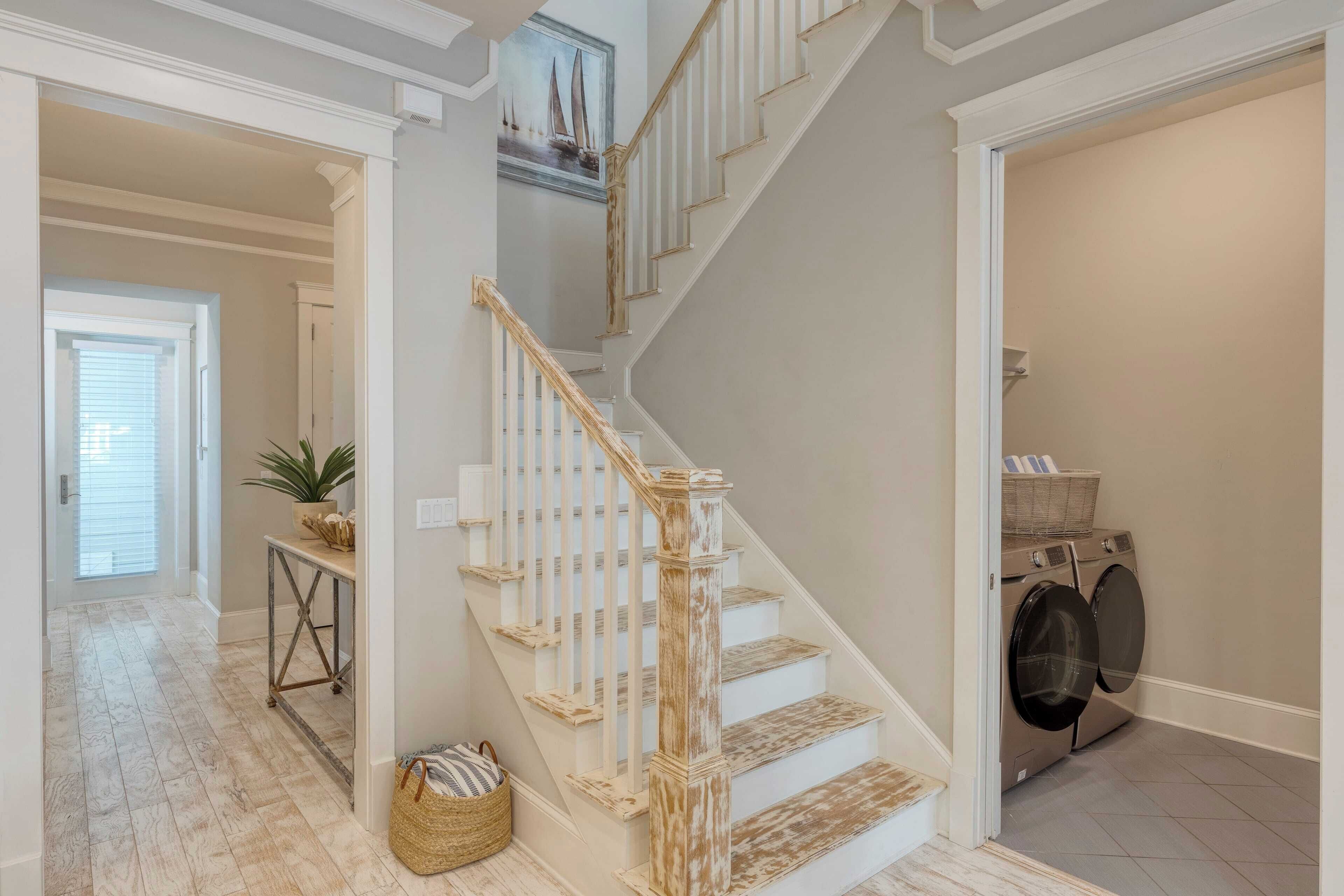 A staircase with white railings and wooden steps, a laundry area with a washing machine, and a hallway with a potted plant and a basket.