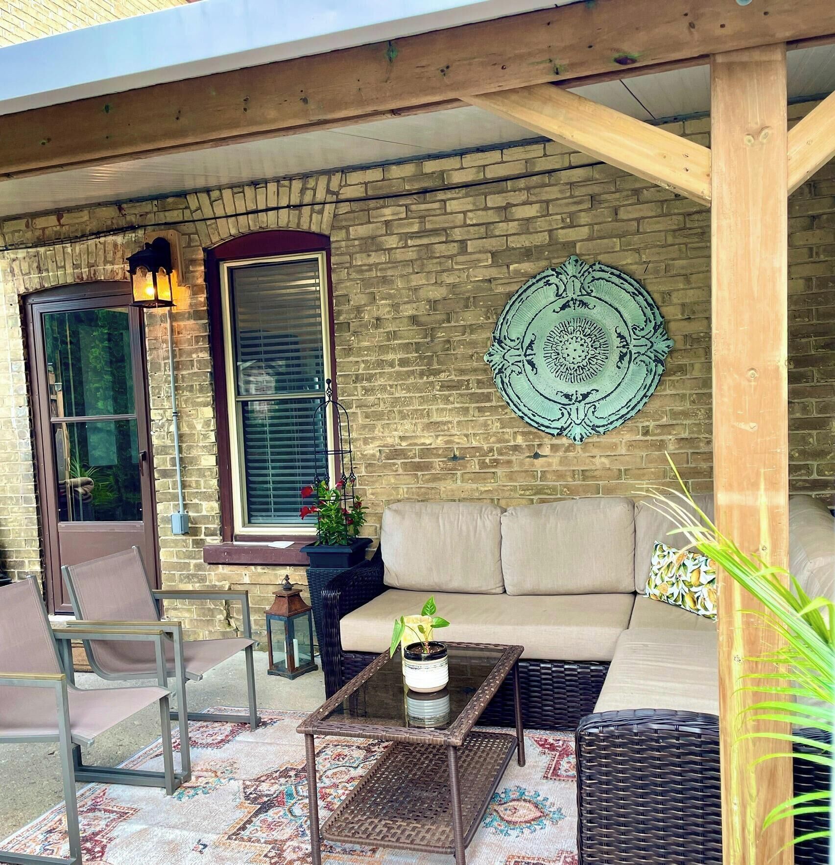 A covered patio area with a brick wall, a cushioned sofa, wicker furniture, and a decorative plate.