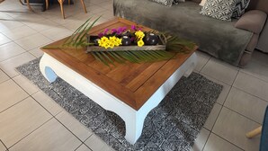 Een woonkamer met een houten salontafel, een bank met gekleurde kussens en een eethoek met een gele tafelkleed.