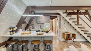 A kitchen with a central island, bar stools, a wooden staircase, and a view of the adjacent bedroom. - Speckled by Avantstay Modern Interior, 0.5mi to Lake! (Kings Beach)