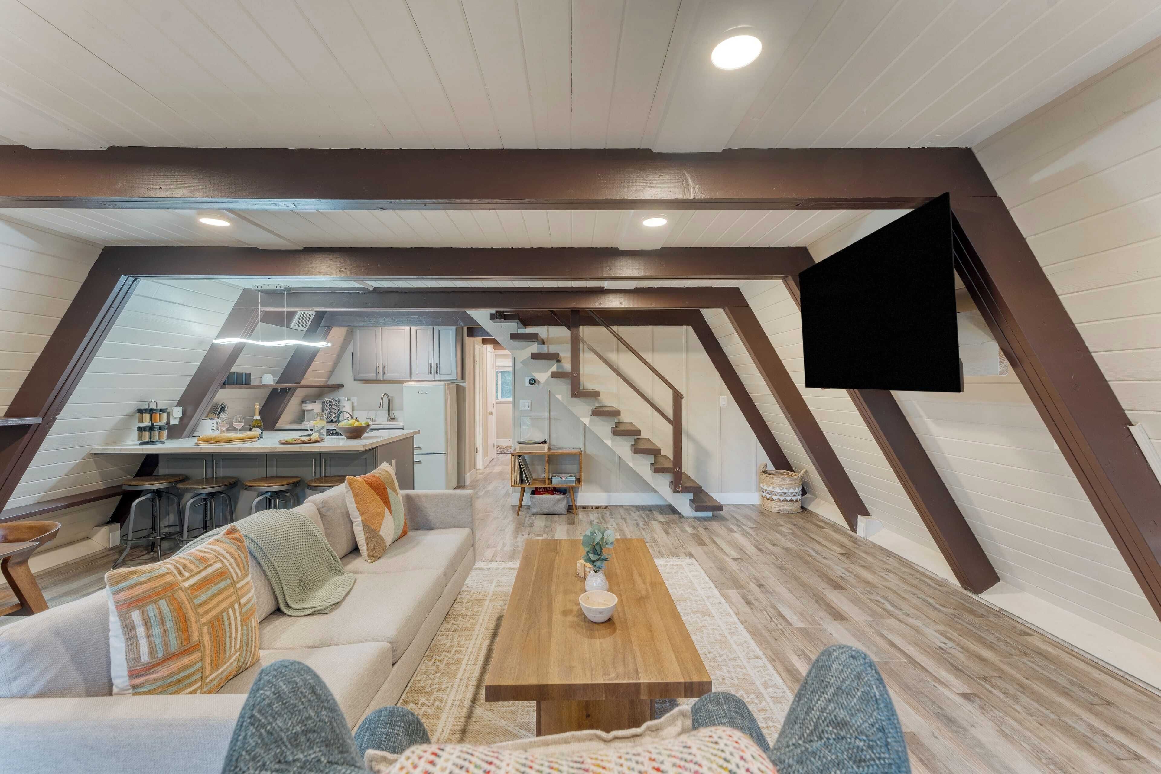Un espacio habitable moderno estilo loft con una mesa de comedor de madera, un sofá y una escalera que conduce a un nivel superior.