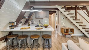 A modern kitchen with a central island, bar stools, wooden beams, and a staircase. - Speckled by Avantstay Modern Interior, 0.5mi to Lake! (Kings Beach)
