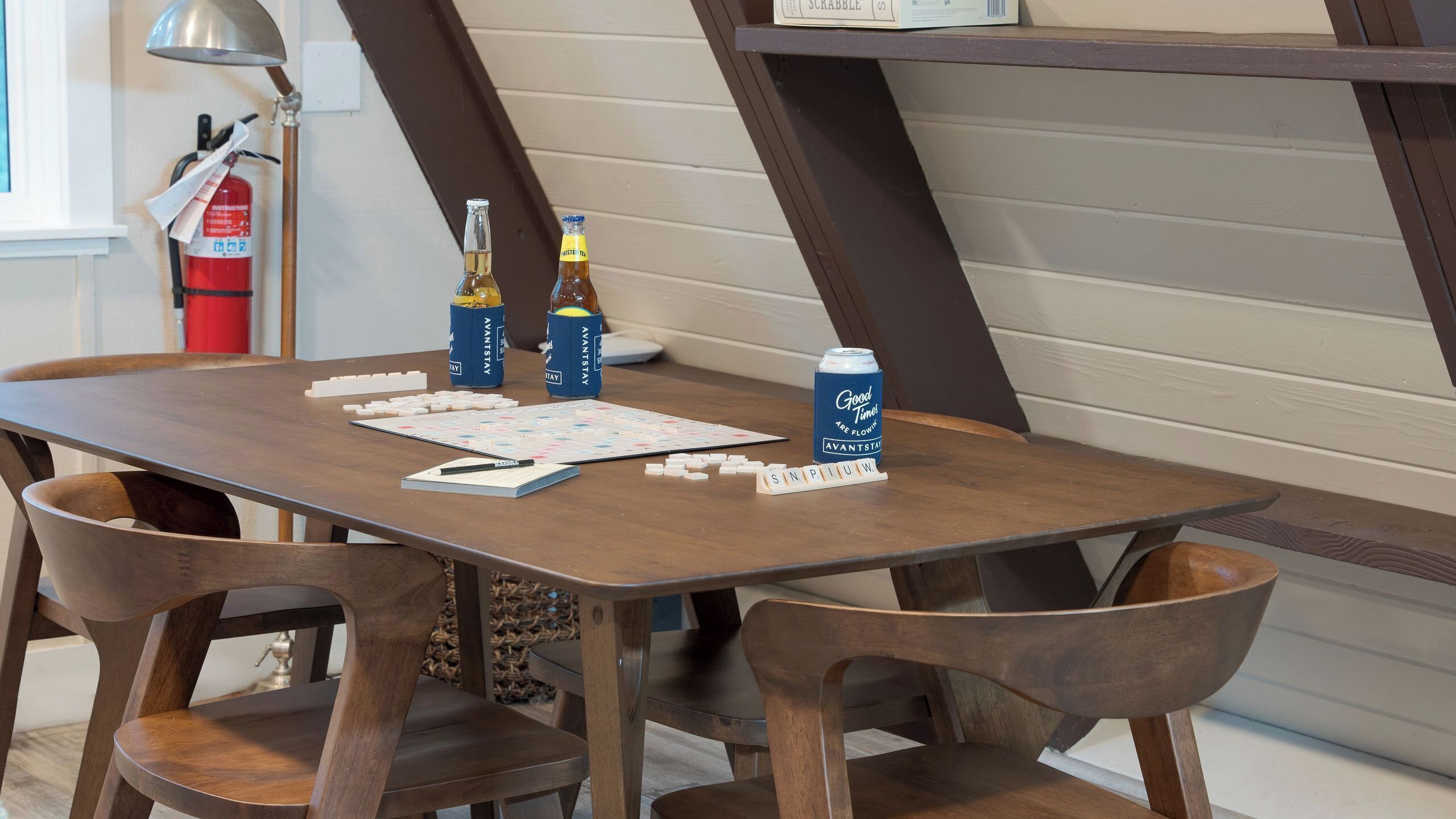 A wooden table with Scrabble tiles, two bottles of beer, and a can of beer.