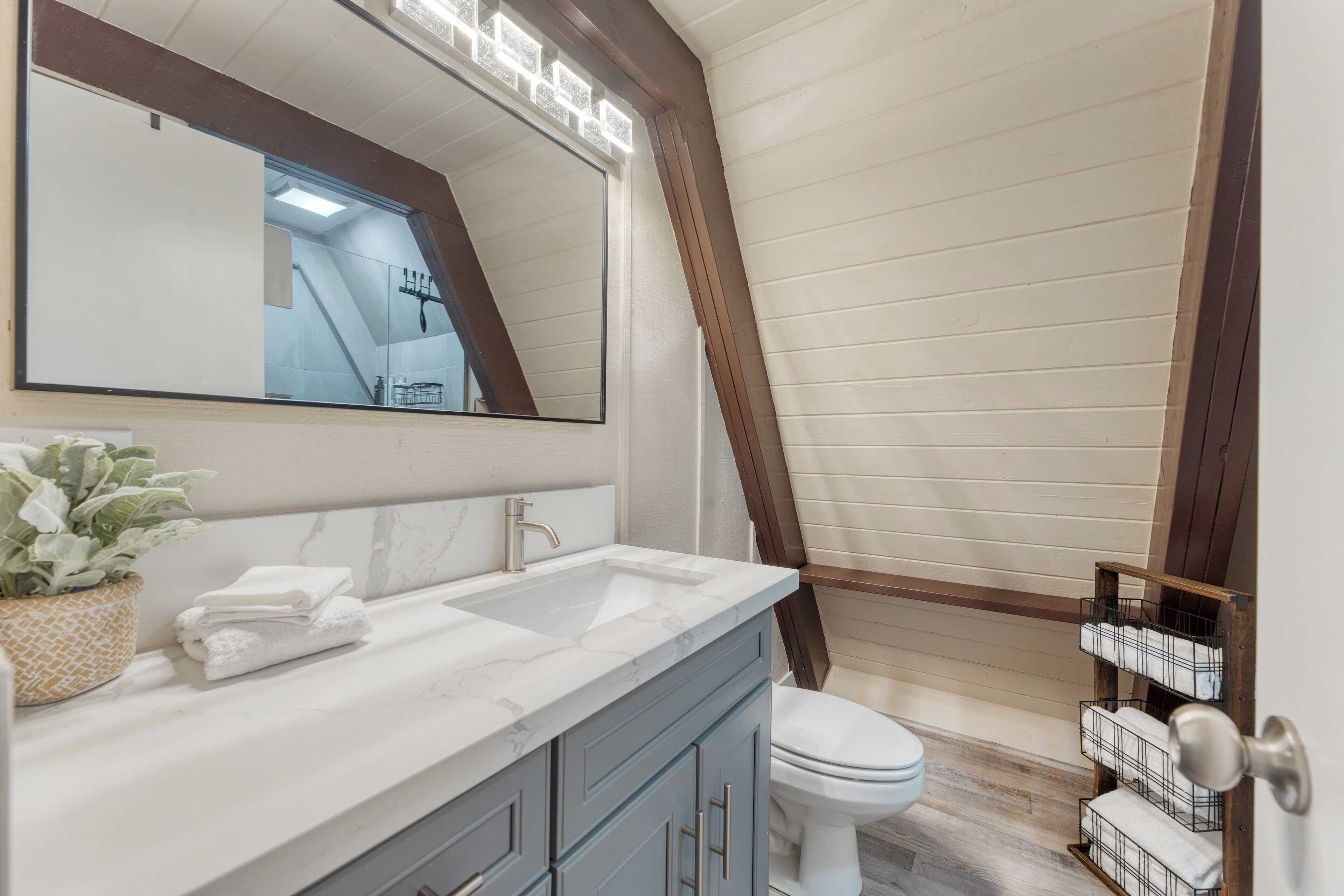 Un baño con lavamanos blanco, armarios azules, un espejo grande y un inodoro blanco.