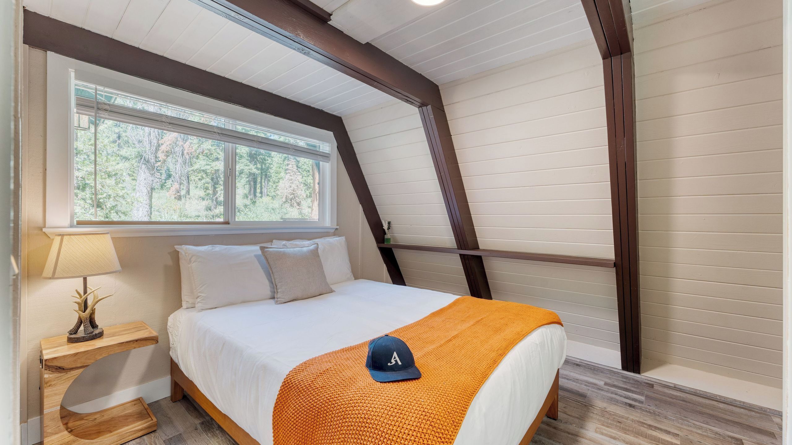 A bedroom with a bed, a nightstand, a lamp, a window, and a view of trees.