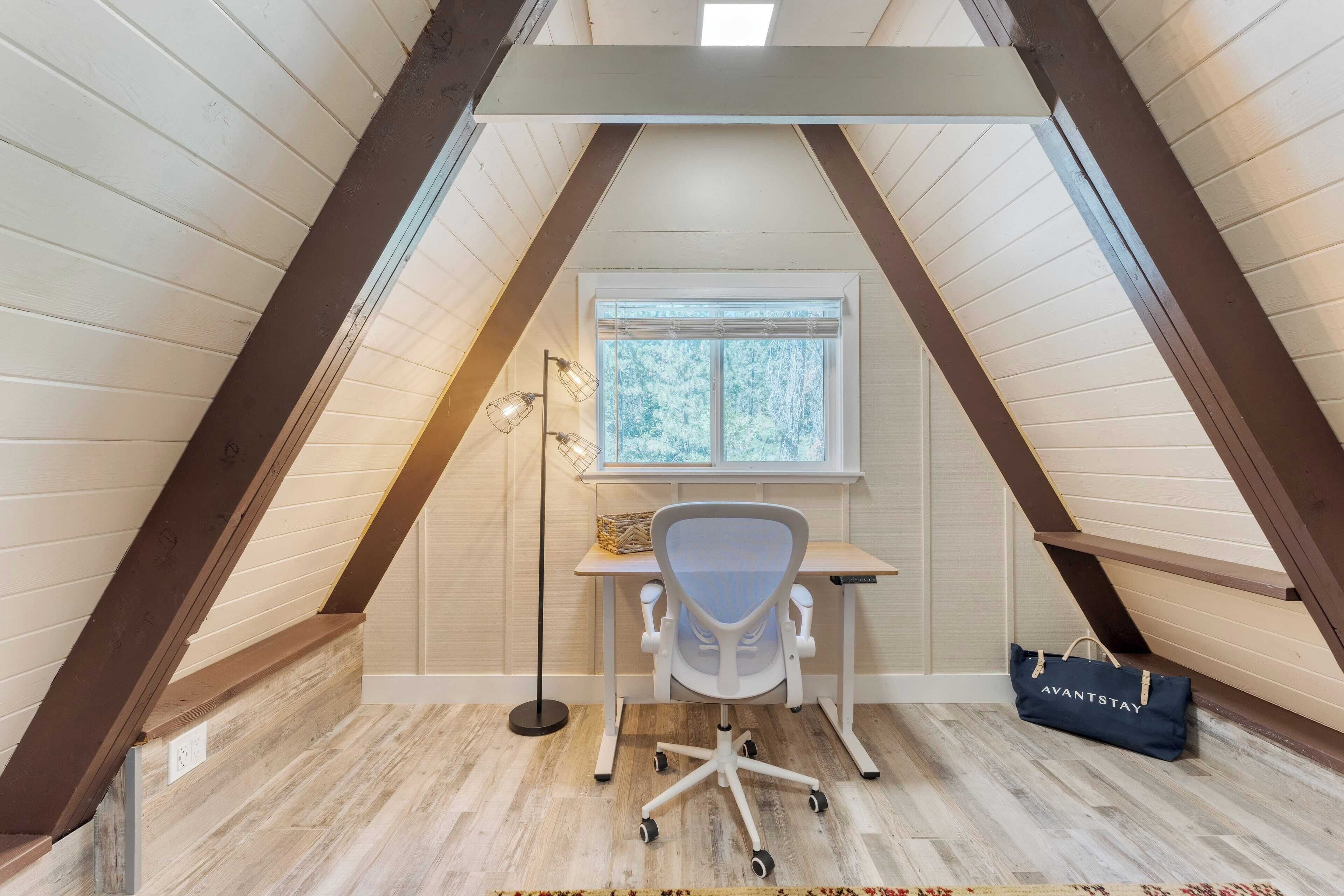A small attic room with a sloped ceiling, a desk with a chair, a window, and a bag on the floor.