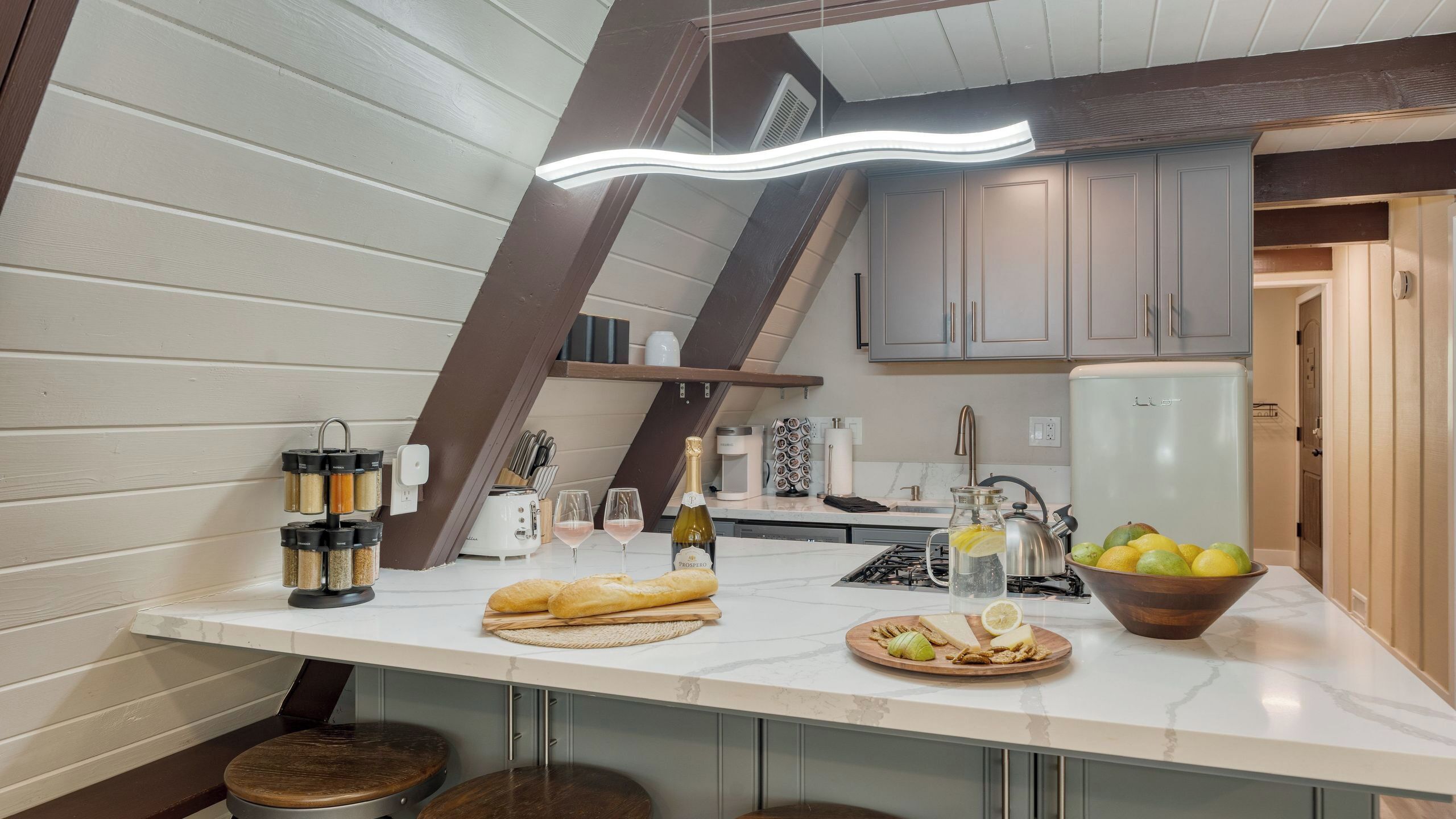 A kitchen with a white countertop, a built-in oven, a sink, and a refrigerator. There are various kitchen items and a bottle of wine on the counter.