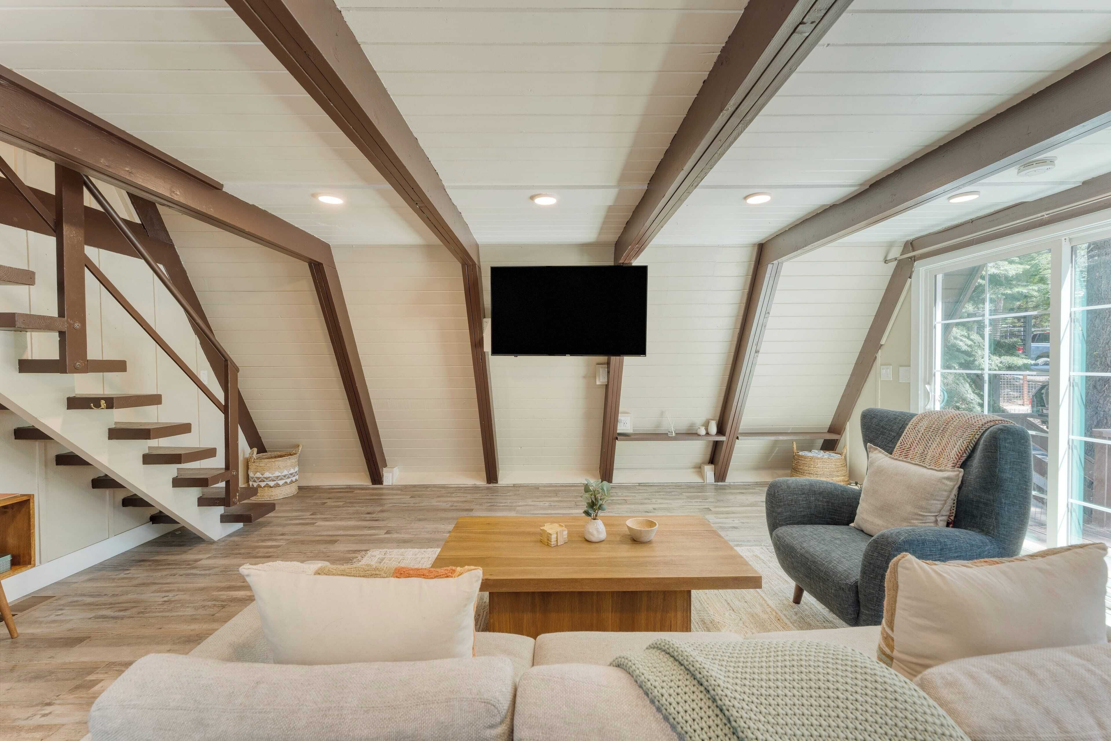 Un vaste salon agrémenté d’un escalier en bois, d’un téléviseur à écran plat fixé au mur et d’une grande fenêtre offrant une vue sur l’extérieur.