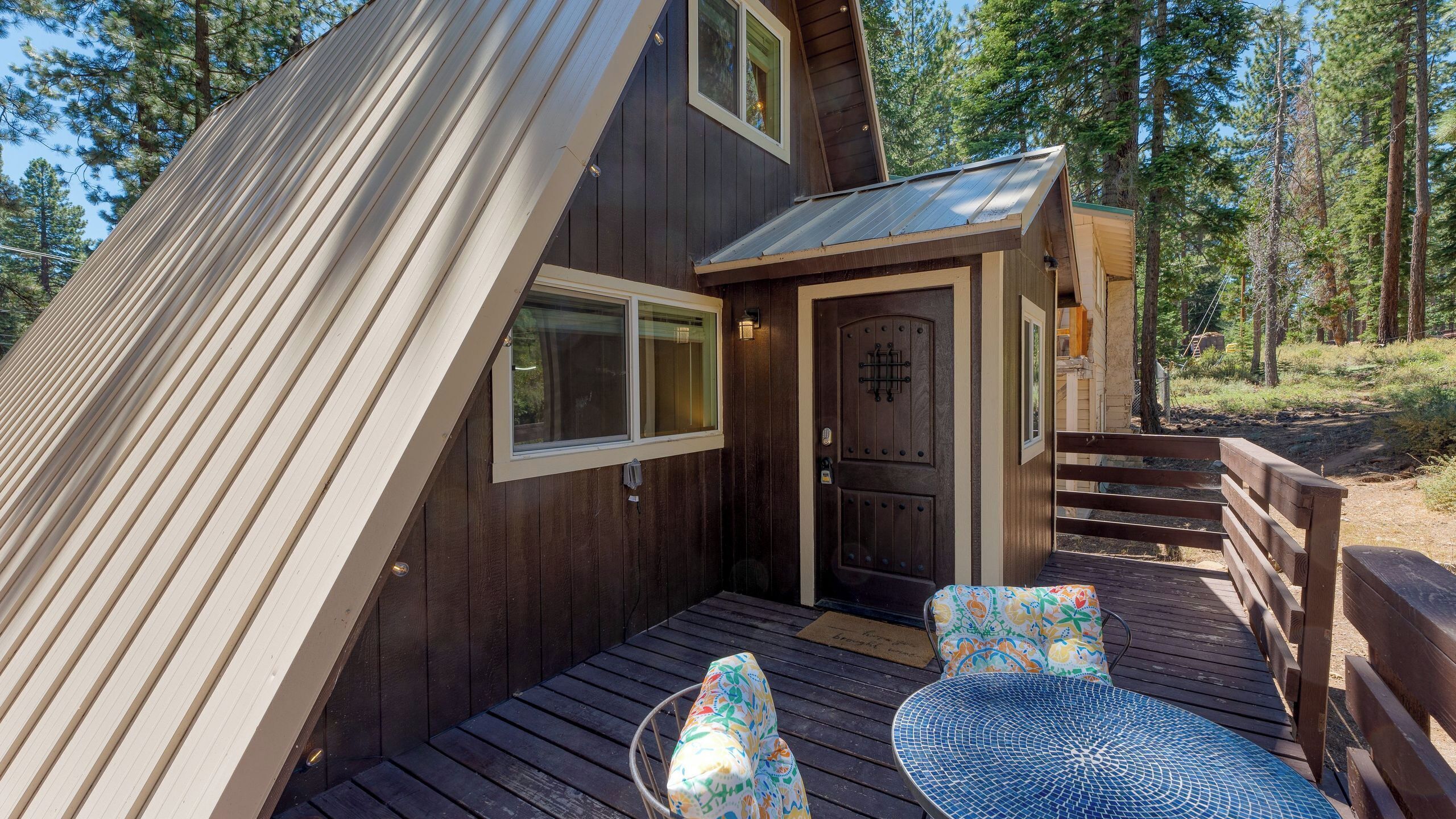 A wooden cabin with a sloped roof, a front door, and a small porch with a bench and a table.