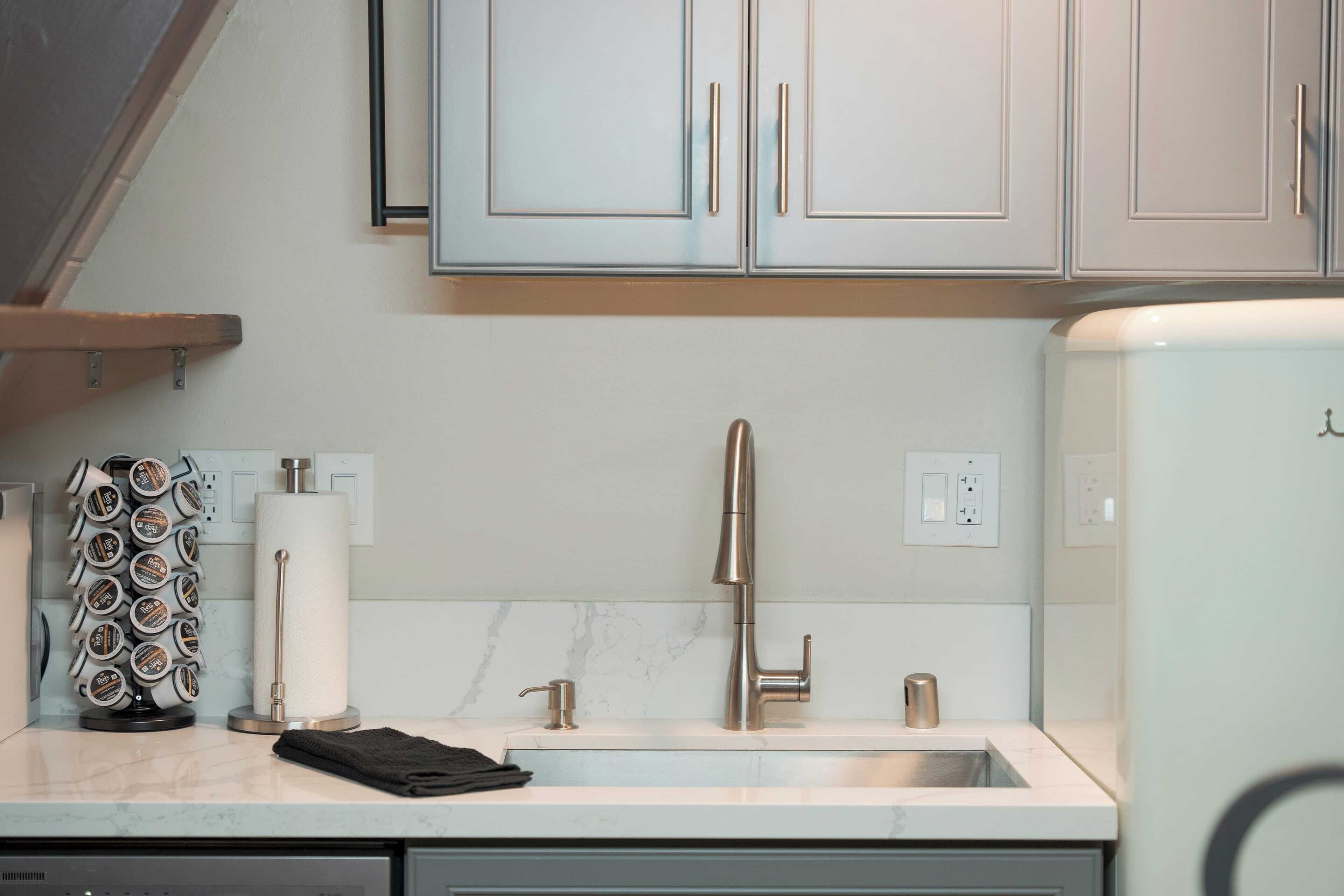 A kitchen with light-colored cabinets, a stainless steel faucet, a paper towel dispenser, and a coffee machine.