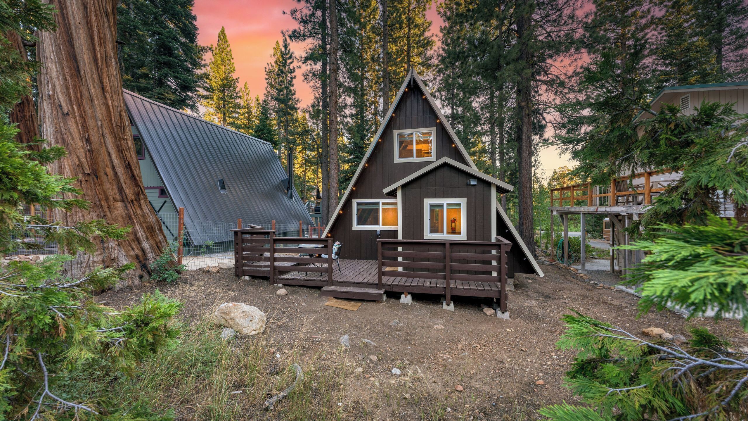 A cabin with a sloped roof, wooden deck, and a fenced entrance.