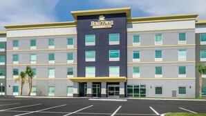 A multi-story hotel with a prominent entrance and a parking lot in front. - HomeTowne Studios by Red Roof Tampa - Airport (Tampa)