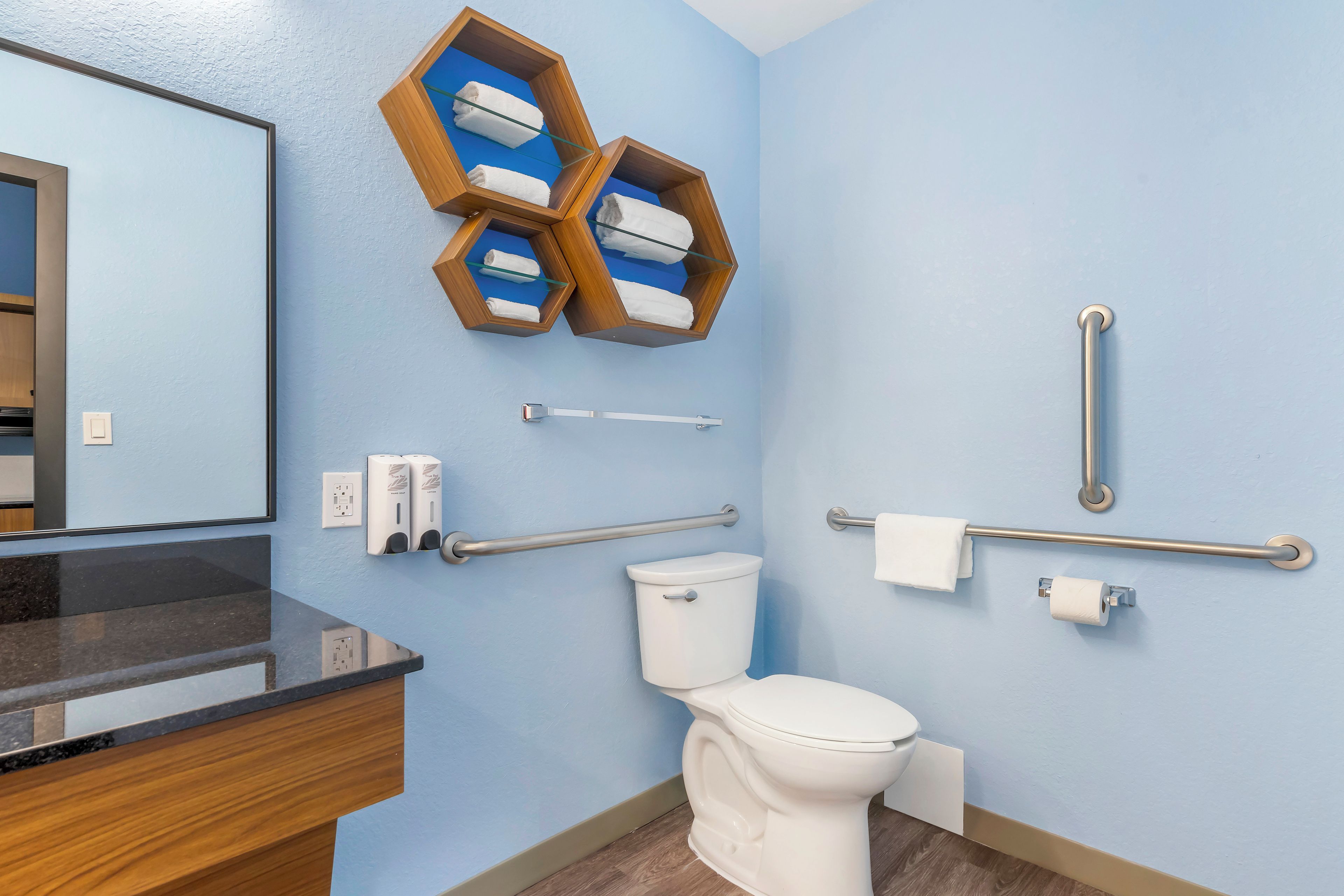 A bathroom with a toilet, hand dryer, towel rack, and a wooden shelf with towels.