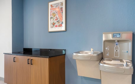A kitchenette with a black countertop and wooden cabinets, a water dispenser, and a framed map on the wall.