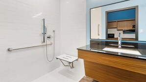 A modern bathroom with a shower, a vanity with a mirror, and a small step for accessibility. - HomeTowne Studios by Red Roof Tampa - Airport (Tampa)