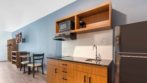 A compact kitchen with wooden cabinetry, a microwave, a stainless steel sink, and a refrigerator. - HomeTowne Studios by Red Roof Tampa - Airport (Tampa)