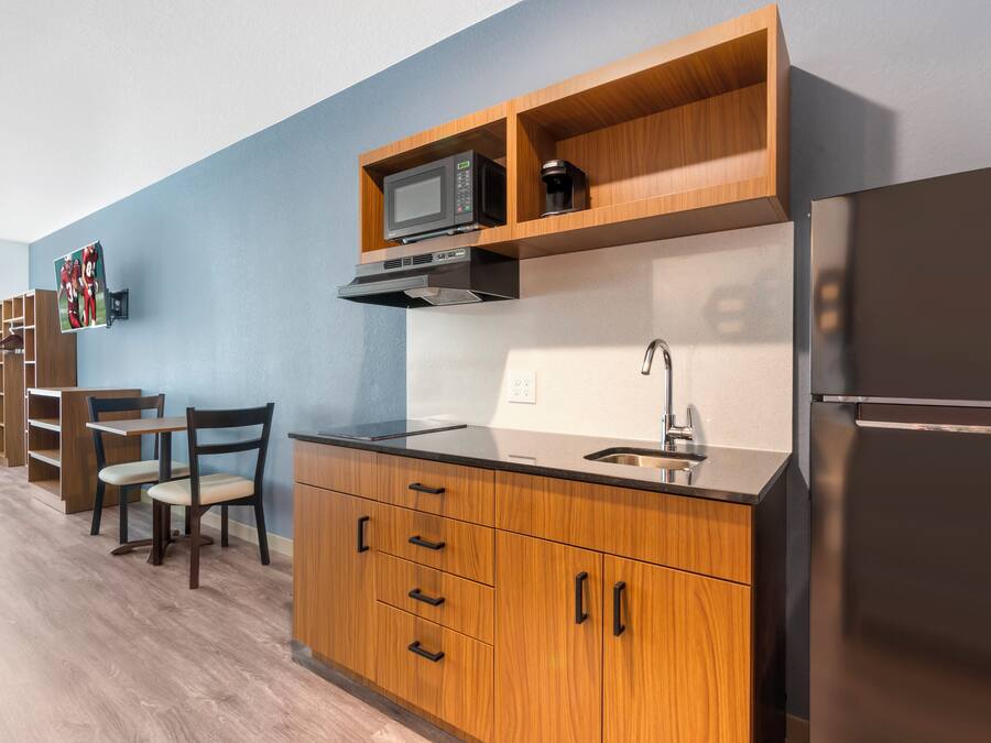 A compact kitchen with wooden cabinetry, a microwave, a stainless steel sink, and a refrigerator.
