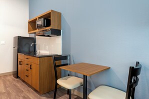 A compact kitchenette with a microwave, stove, and sink, a small wooden table, and a chair. - HomeTowne Studios by Red Roof Tampa - Airport (Tampa)