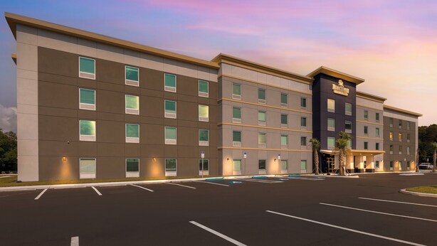 A multi-story hotel with a flat facade, large windows, and a parking lot in front. - HomeTowne Studios by Red Roof Tampa - Airport (Tampa)