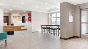 A reception area with a counter, a wooden bench, and a seating area with chairs. - HomeTowne Studios by Red Roof Tampa - Airport (Tampa)