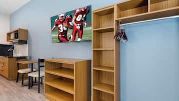 A room with a wooden desk, a chair, a television mounted on the wall, and built-in shelving units.