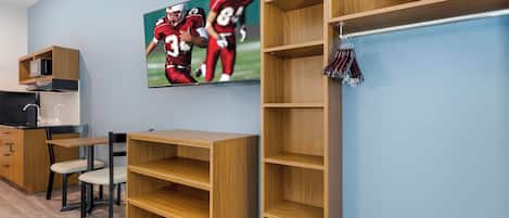 A room with a wooden desk, a chair, a television mounted on the wall, and built-in shelving units.