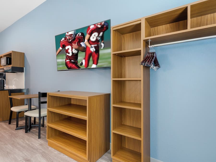 A room with a wooden desk, a chair, a television mounted on the wall, and built-in shelving units.