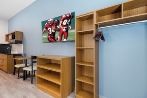 A room with a wooden desk, a chair, a television mounted on the wall, and built-in shelving units. - HomeTowne Studios by Red Roof Tampa - Airport (Tampa)