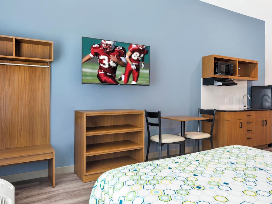 Ein Hotelzimmer mit Bett, Schreibtisch, Stuhl, Wandfernseher und einer Küchenzeile.