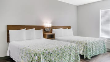 A hotel room with two beds, a nightstand with a lamp, and a window with blinds.