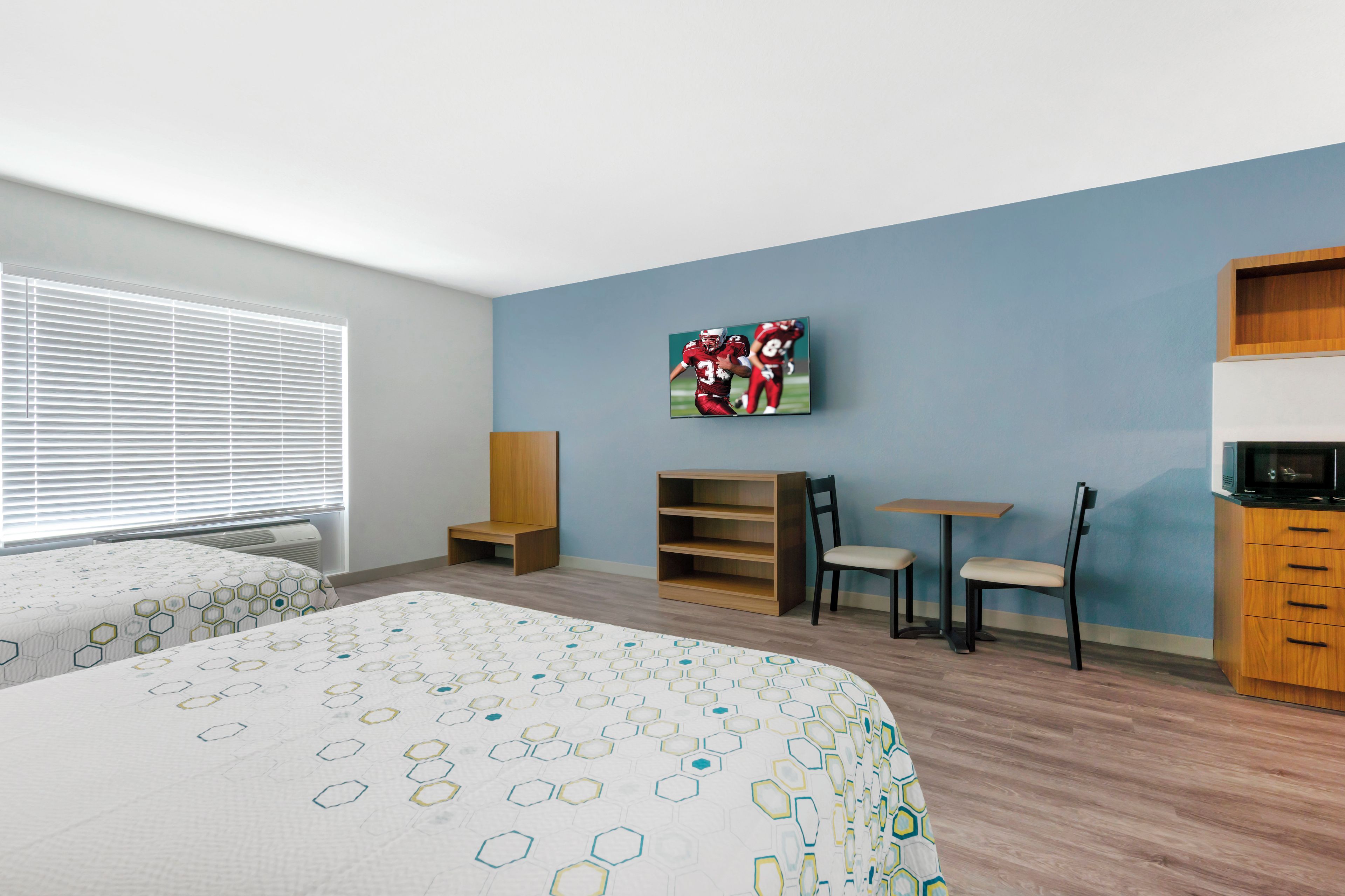 A hotel room with two beds, a television mounted on the wall, a wooden cabinet, and a small table with chairs.
