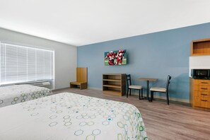 A hotel room with two beds, a television mounted on the wall, a wooden cabinet, and a small table with chairs.