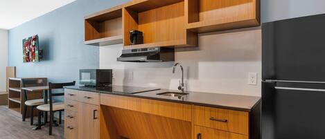A modern kitchen with wooden cabinets, a black refrigerator, a microwave, and a coffee maker.