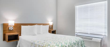 Una habitación de hotel con una cama, dos mesitas de noche con lámparas, una ventana con persianas y un aire acondicionado instalado en la pared.