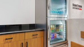A kitchen with a stainless steel refrigerator, wooden cabinets, and a glass door freezer. - HomeTowne Studios by Red Roof Tampa - Airport (Tampa)