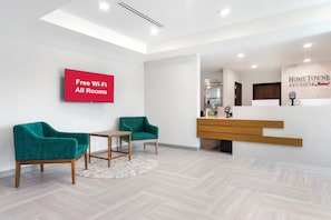 Un área de recepción moderna con un cartel que dice 'Wi-Fi gratuito en todas las habitaciones', una mesa de recepción y sillas color turquesa.