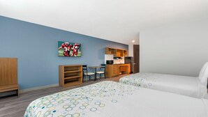 A hotel room with two beds, a desk, a chair, a bookshelf, and a kitchen area. - HomeTowne Studios by Red Roof Tampa - Airport (Tampa)