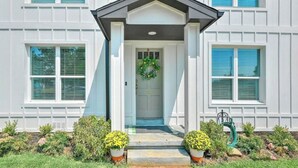 A modern two-story house with a front porch, a door with a wreath, and a garden with potted plants. - Downtown Denison Dream (Denison)