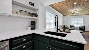 A modern kitchen with white countertops, dark green cabinets, and a wooden ceiling. - Downtown Denison Dream (Denison)