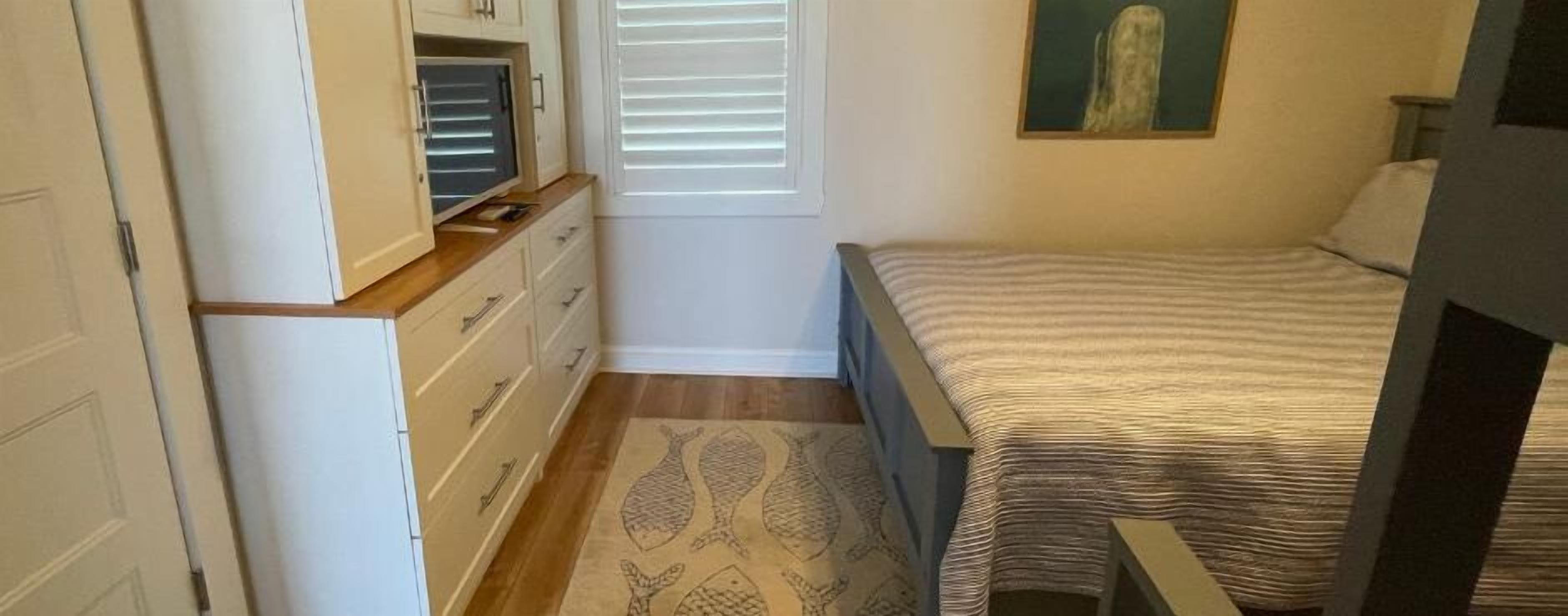 Un dormitorio con cama, cómoda, ventana con persianas y un cuadro en la pared.